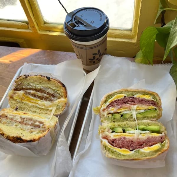 Two Olivier Cafe breakfast sandwiches with melted cheese and a coffee cup by a window.