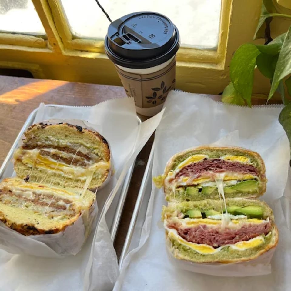 Two Olivier Cafe breakfast sandwiches with melted cheese and a coffee cup by a window.