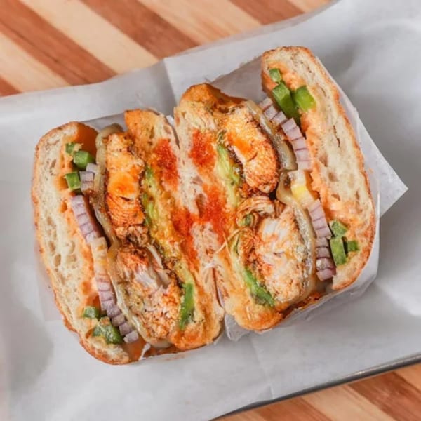 A toasted Olivier Cafe sandwich with chicken, avocado, cheese, and red sauce on white paper.