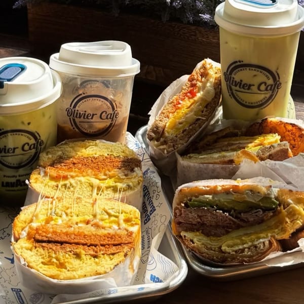 Olivier Cafe sandwiches and iced drinks on trays, with melted cheese stretching from a sandwich.