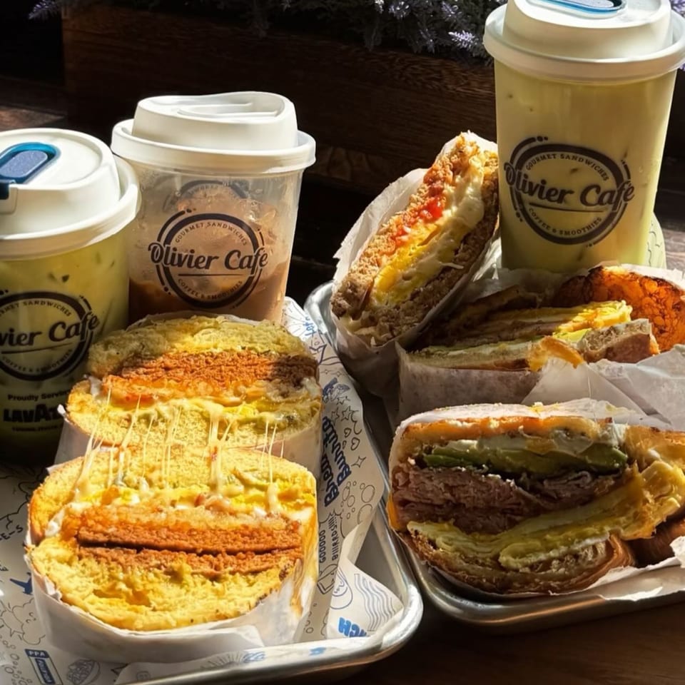 Olivier Cafe sandwiches and iced drinks on trays, with melted cheese stretching from a sandwich.