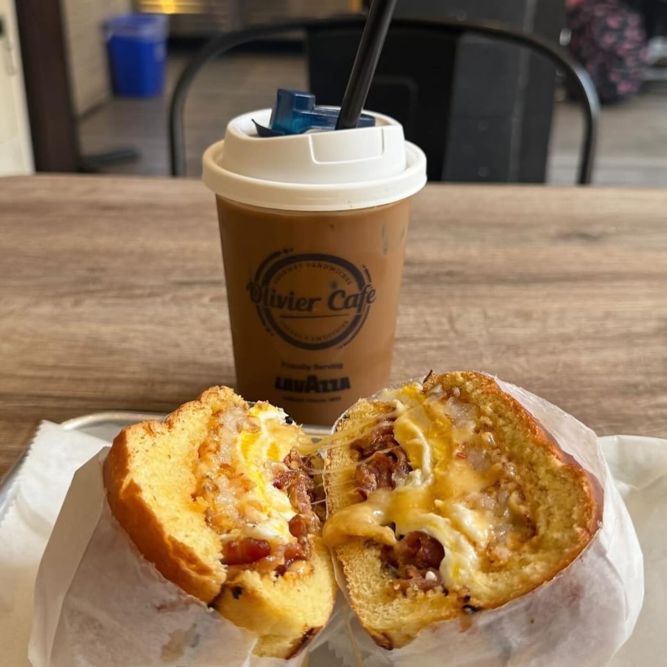 A breakfast sandwich with melted cheese and egg, next to an iced coffee from Olivier Cafe.
